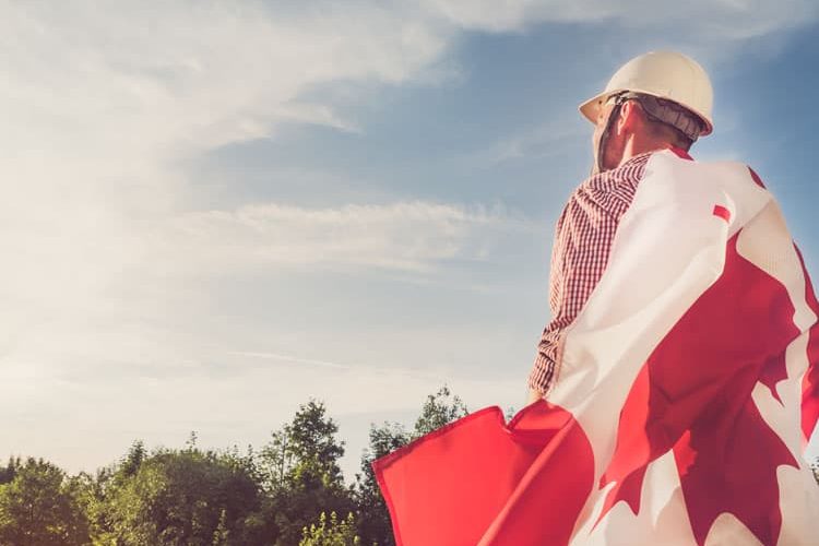 Attractive engineer, holding an Canadian Flag in the park against the backdrop of green trees and the setting sun, looking into the distance. Close-up. Concept of labor and employment